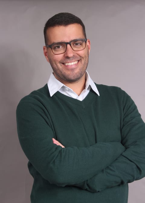 Tiago Martins Peres smiling, arms crossed, in a green sweater over a white shirt